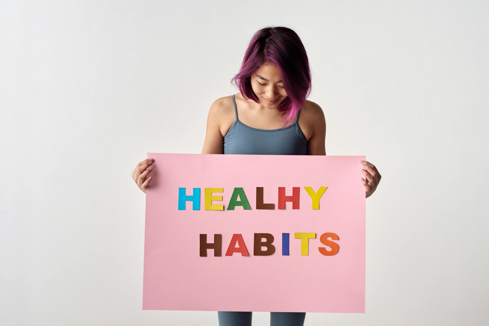 Asian woman holding a colorful 'Healthy Habits' sign in a studio setting, promoting wellness.